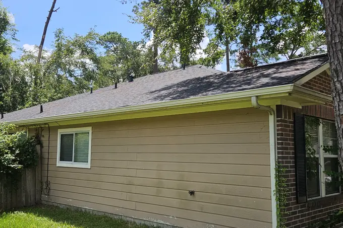 Shingle roof edge and white gutter above a tan wall